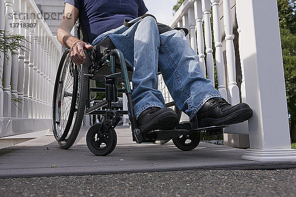 Mann mit Querschnittslähmung im Rollstuhl auf der Rampe zum Haus
