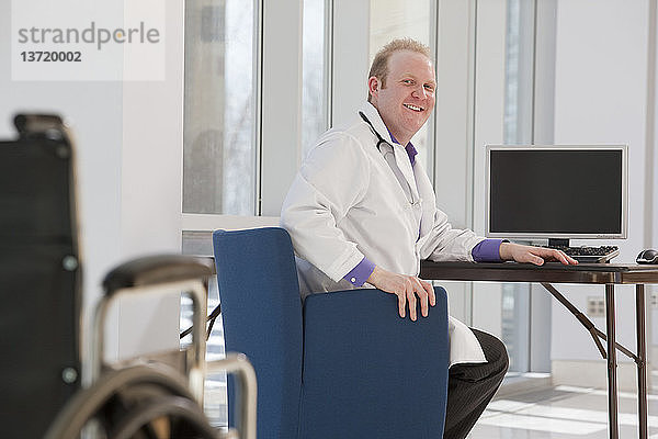 Arzt sitzt vor einem Computer und lächelt
