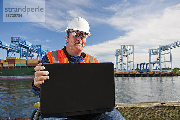 Transportingenieur im Rollstuhl  der im Verschiffungshafen Daten auf einem Laptop aufzeichnet