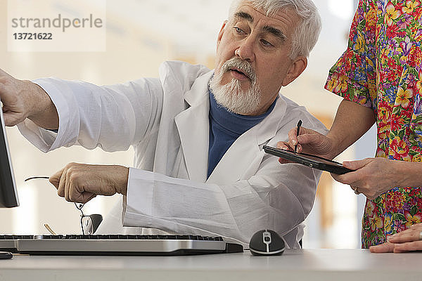 Arzt und Krankenschwester in einer Konferenz mit Computer und Tablet