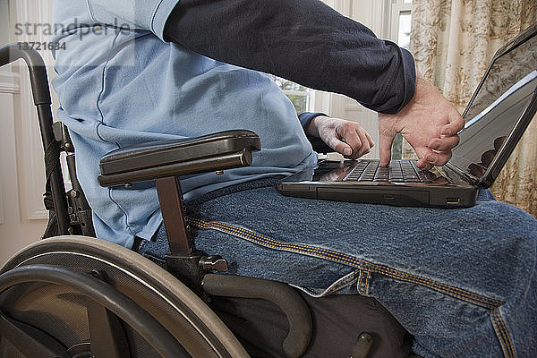 Geschäftsmann mit Querschnittslähmung im Rollstuhl  der mit behinderten Händen an einem Laptop arbeitet