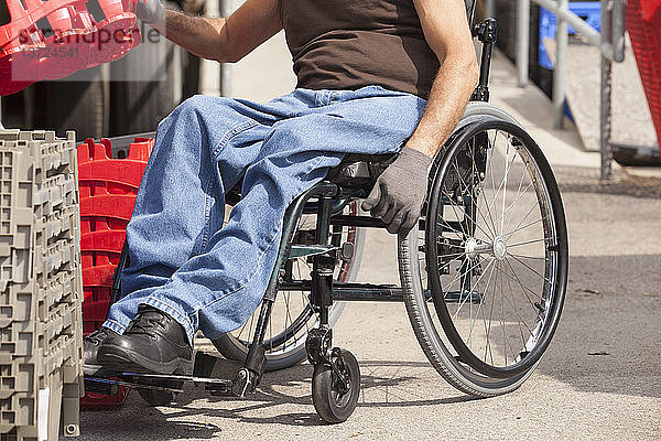 Laderampenarbeiter mit Rückenmarksverletzung im Rollstuhl beim Stapeln von Lagerbehältern