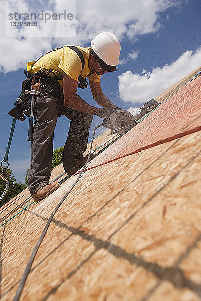 Zimmermann bei der Arbeit mit einer Kreissäge an einer Dachplatte auf einer Baustelle für ein Haus