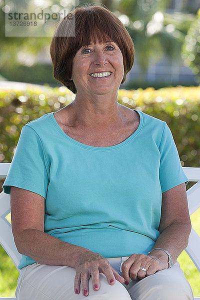 Porträt einer älteren Frau  die in einem Park sitzt und lächelt