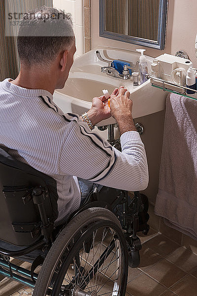 Mann mit Rückenmarksverletzung im Rollstuhl nimmt Medikamente ein