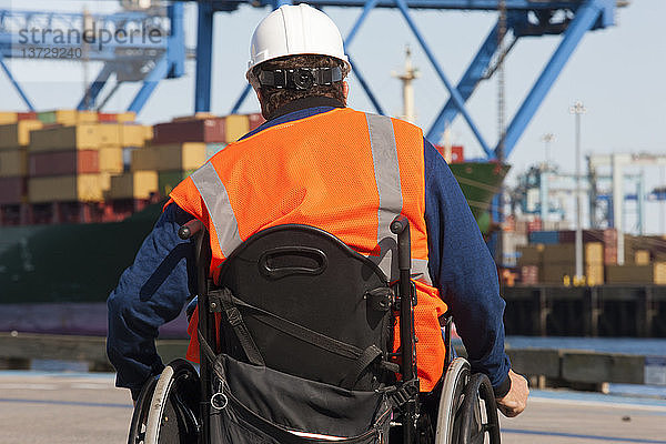 Transportingenieur im Rollstuhl bei der Inspektion von Schiffscontainern und Containerkränen im Verschiffungshafen