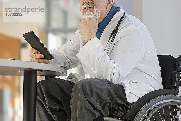 Arzt mit Muskeldystrophie im Rollstuhl schaut auf sein Tablet