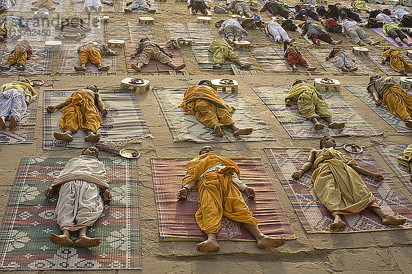Schüler einer Sanskrit-Schule bei ihrer täglichen Yogastunde bei Sonnenaufgang auf dem Ghat von Varanasi. Hier nehmen sie die Savasana-Haltung (Körperhaltung) ein