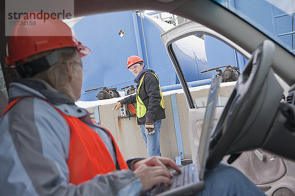 Ingenieur mit Laptop im Lkw mit einem anderen Ingenieur  der die Baustelle inspiziert