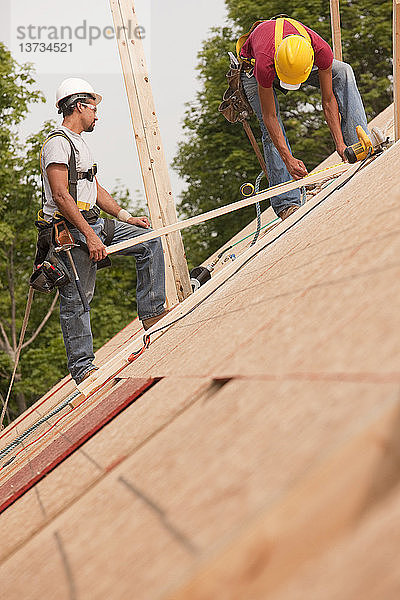 Hispanische Zimmerleute messen die Bretter auf dem Dach eines im Bau befindlichen Hauses aus