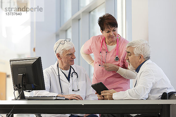 Arzt mit Muskeldystrophie im Rollstuhl im Gespräch mit einem Arzt und einer Krankenschwester