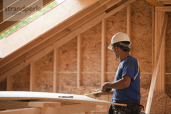 Ein spanischer Zimmermann misst ein Stück Ummantelung an einem im Bau befindlichen Haus aus