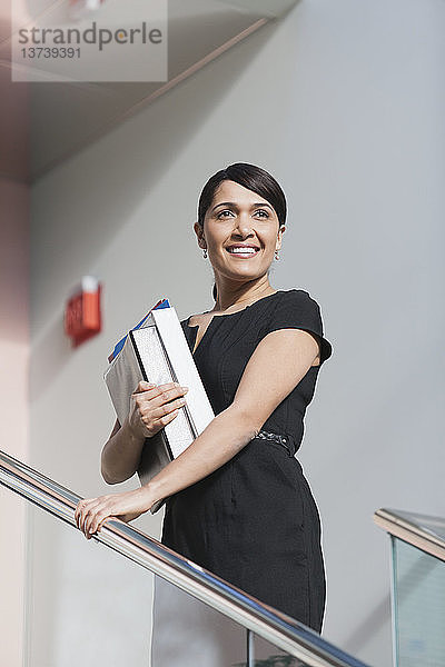 Geschäftsfrau mit Aktenordnern auf der Treppe eines Bürogebäudes