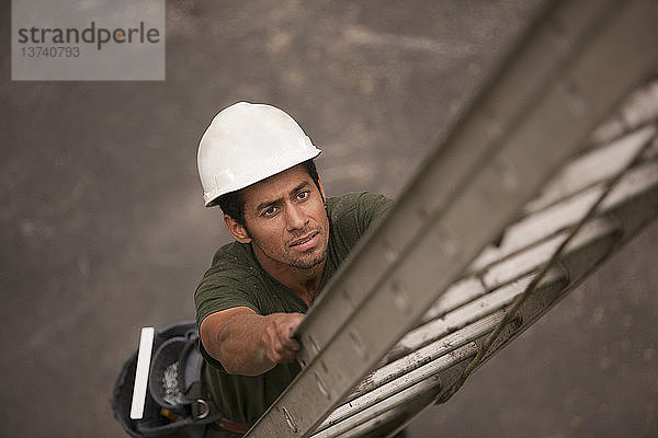 Hochformatige Ansicht eines Zimmermanns  der auf einer Baustelle auf eine Leiter steigt