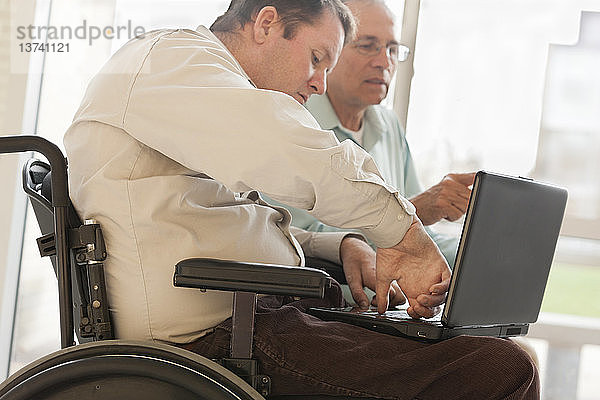 Tetraplegiker mit Rückenmarksverletzung im Rollstuhl tippt mit dem Daumen auf dem Computer