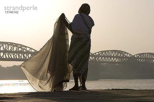Frau entfaltet einen Sari entlang des Flusses Ganga