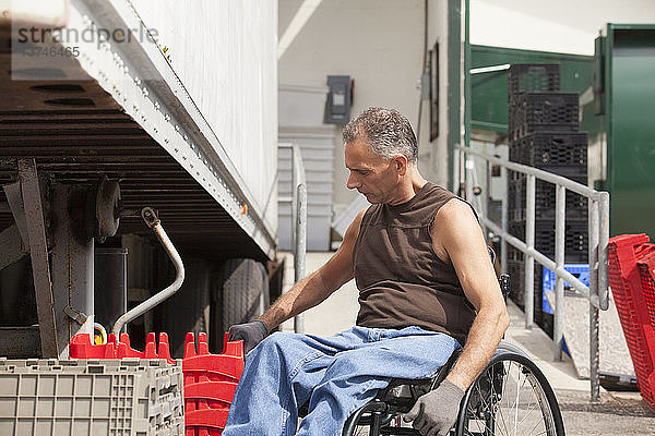 Laderampenarbeiter mit Rückenmarksverletzung im Rollstuhl beim Stapeln von Lagerbehältern