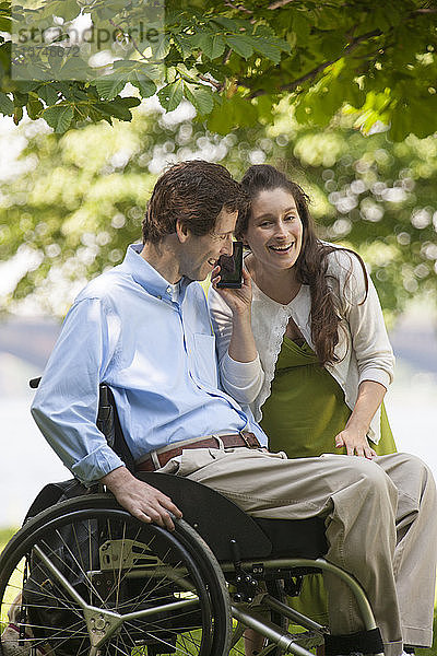 Schwangere Frau hört mit ihrem Mann  der im Rollstuhl sitzt und eine Rückenmarksverletzung hat  auf dem Smartphone