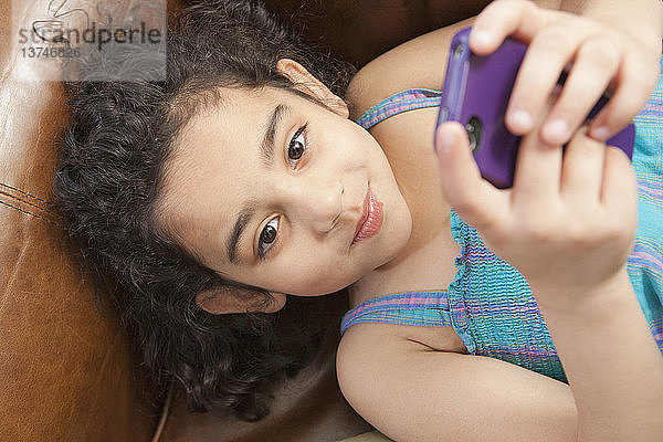 Hispanisches Mädchen  das auf einer Couch liegt und sich eine Textnachricht auf einem Mobiltelefon ansieht