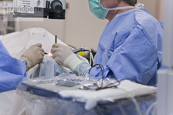 Chirurgische Technikerin  die das Auge spült  und Arzt  der während einer Kataraktoperation ein Phako mit einem Cracker-Instrument verwendet