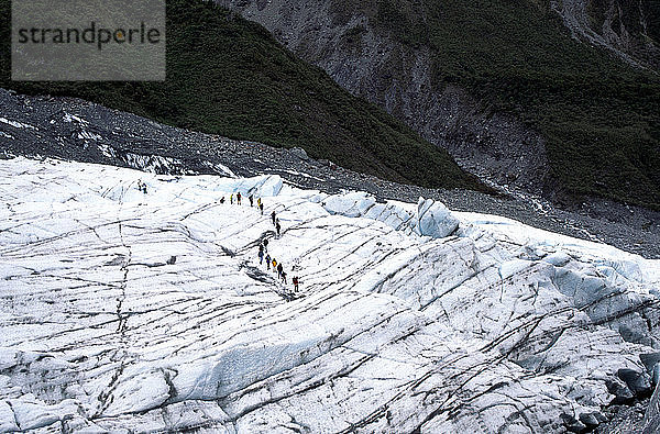 Menschen  die auf Gletschereis gehen  das von Moränensedimenten umgeben ist  die vom Fox-Gletscher transportiert wurden  Neuseeland