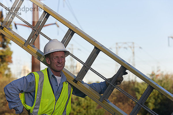 Ingenieur  der eine Leiter hält  um Geräte an Strommasten zu installieren