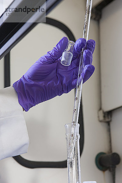 Laborwissenschaftler  der eine Pipette benutzt  um ein Reagenz für eine chemische Analyse hinzuzufügen