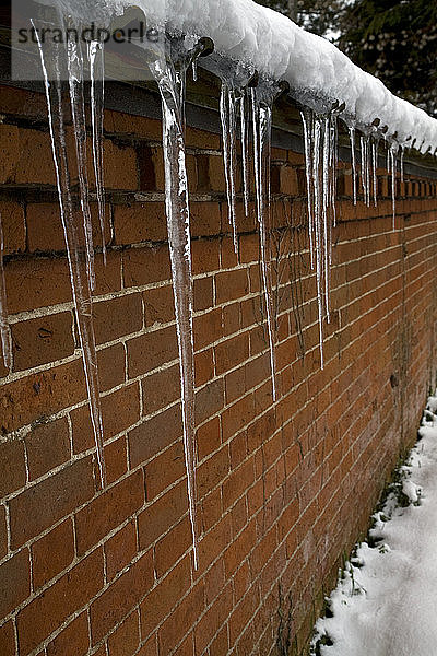 Eiszapfen hängen an einer roten Backsteinmauer herunter