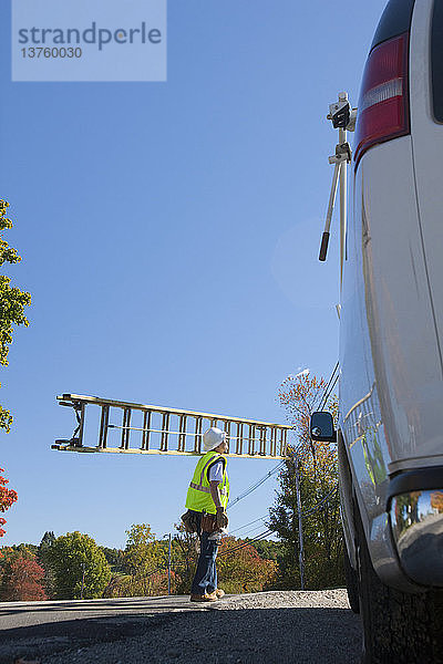 Ingenieur trägt eine Leiter  um einen Strommast zu besteigen