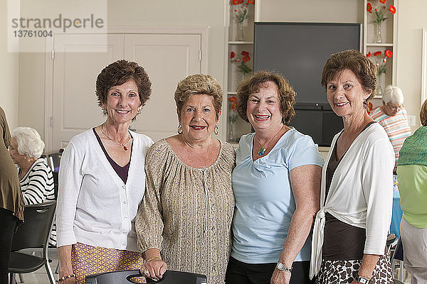 Porträt von vier älteren Freundinnen  die bei einem Mittagessen lächeln