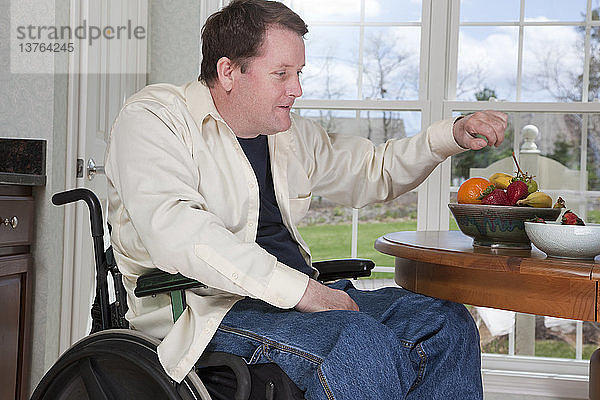 Mann mit Rückenmarksverletzung im Rollstuhl isst zu Hause frisches Obst