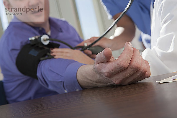 Ärztin und Krankenschwester messen den Blutdruck eines Patienten