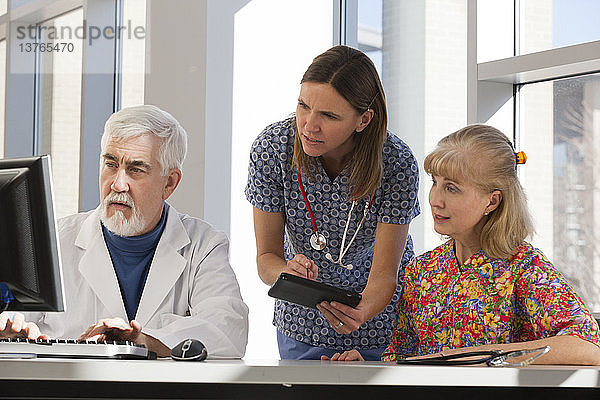 Zwei Krankenschwestern und ein Arzt arbeiten an Computer und Tablet