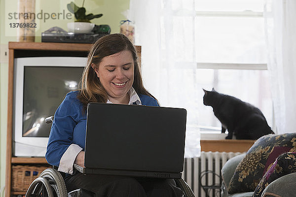 Geschäftsfrau mit Spina bifida im Rollstuhl benutzt zu Hause einen Laptop