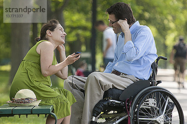 Schwangere Frau mit einem querschnittsgelähmten Ehemann im Rollstuhl  der einem MP3-Player zuhört