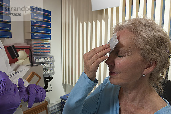 Patientin  die nach einer Botox-Behandlung Eis auf ihre Stirn legt