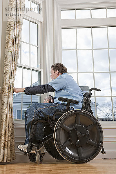 Ein querschnittsgelähmter Mann im Rollstuhl schaut aus dem Fenster seiner barrierefreien Wohnung