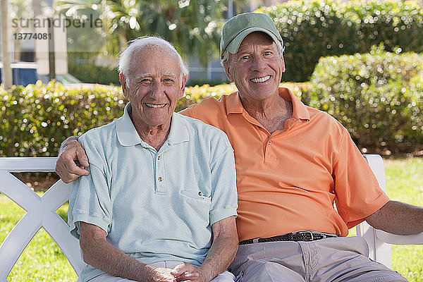 Porträt von zwei älteren Männern  die auf einer Parkbank sitzen und lächeln