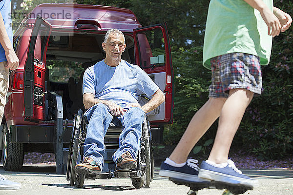 Mann mit Querschnittslähmung im Rollstuhl beobachtet seinen Sohn auf dem Skateboard