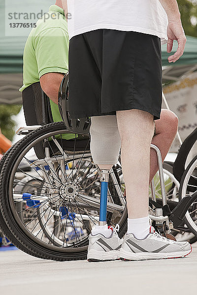 Mann mit Beinprothese steht neben einem Mann im Rollstuhl mit Rückenmarksverletzung
