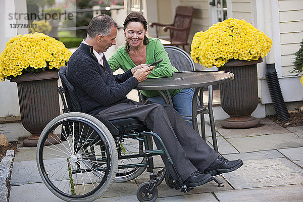 Frau und ihr Mann im Rollstuhl sitzen in einem Café und benutzen ein digitales Tablet