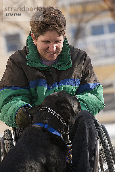 Frau mit Multipler Sklerose spielt im Winter mit einem Diensthund