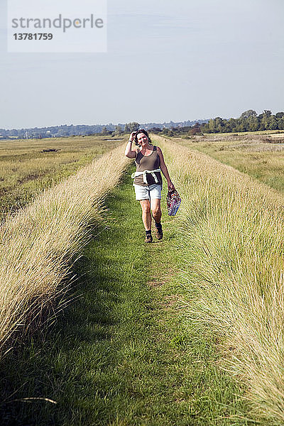 Frau beim Spazierengehen am Hochwasserschutzufer  Fluss Deben  Sutton  Suffolk