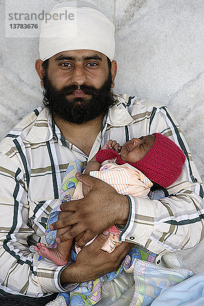 Sikh-Vater hält sein Baby im Bangla Sahib Gurdwara  Neu-Delhi