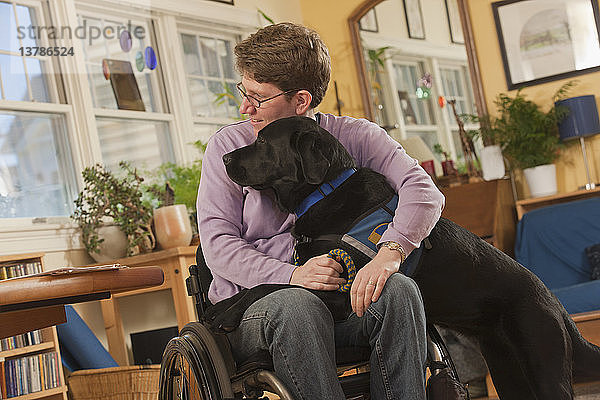 Frau mit Multipler Sklerose im Rollstuhl umarmt ihren Diensthund