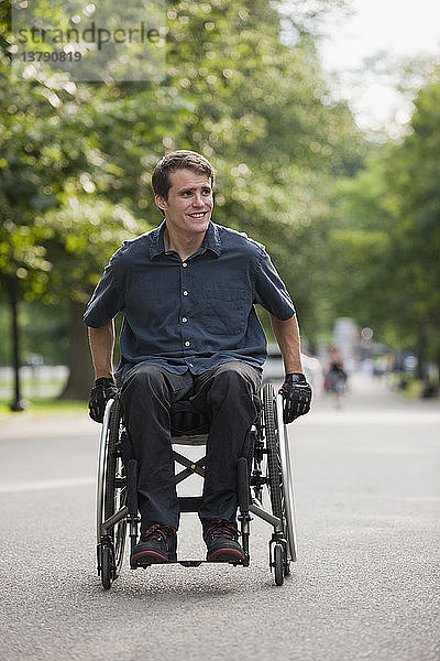 Ein Mann mit einer Rückenmarksverletzung im Rollstuhl manövriert seinen Rollstuhl auf einem Weg durch einen öffentlichen Park