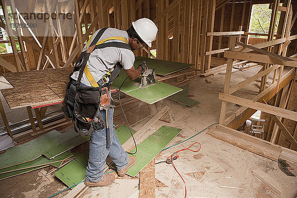 Zimmermann bei der Arbeit mit einer Kreissäge an einer Außenwandverkleidung in einem im Bau befindlichen Haus