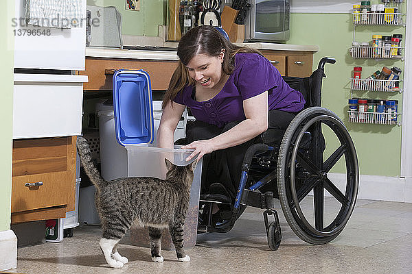 Frau mit Spina Bifida im Rollstuhl füttert eine Katze in der barrierefreien Küche