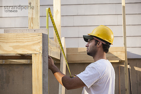 Hispanischer Zimmermann misst Terrassenbalken mit einziehbarem Lineal