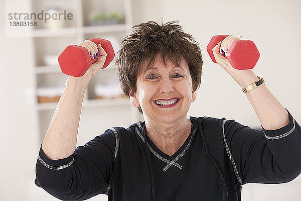 Porträt einer älteren Frau  die mit Hanteln in einem Fitnessstudio trainiert